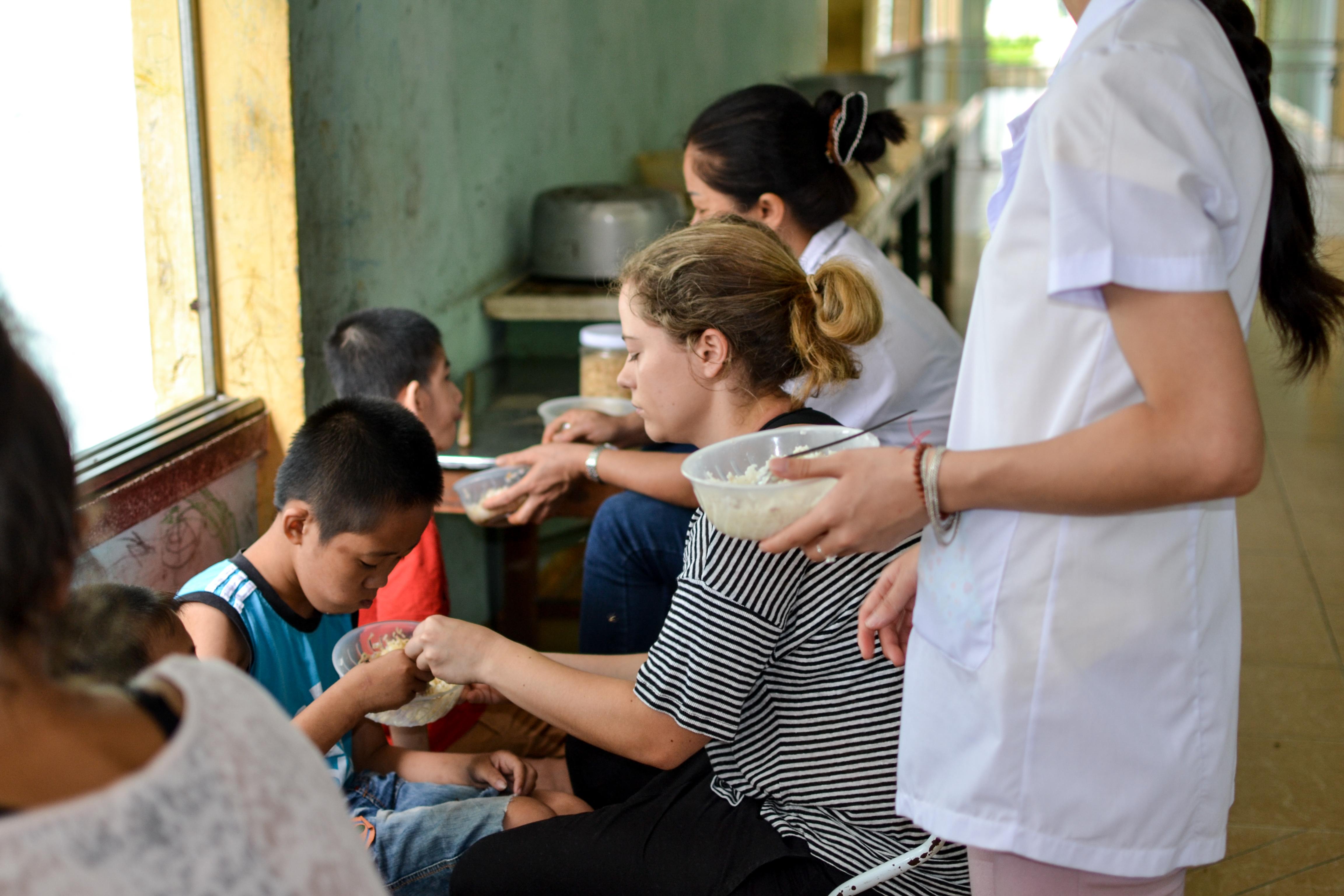A Projects Abroad intern on her occupational therapy internship in Vietnam is helping a young boy eat his food and gaining internation work experience. Pictured here is a Projects Abroad intern helping a young boy learn how to eat with limited arm movement whilst she undertakes her occupational therapy internship in Vietnam.